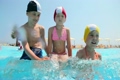 Boy and girls sitting in the pool, the boy splashes water 
