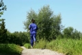 man in turn blue gym suits runs forward on lane in park in summer