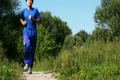 man in turn blue gym suits runs on lane in park in summer